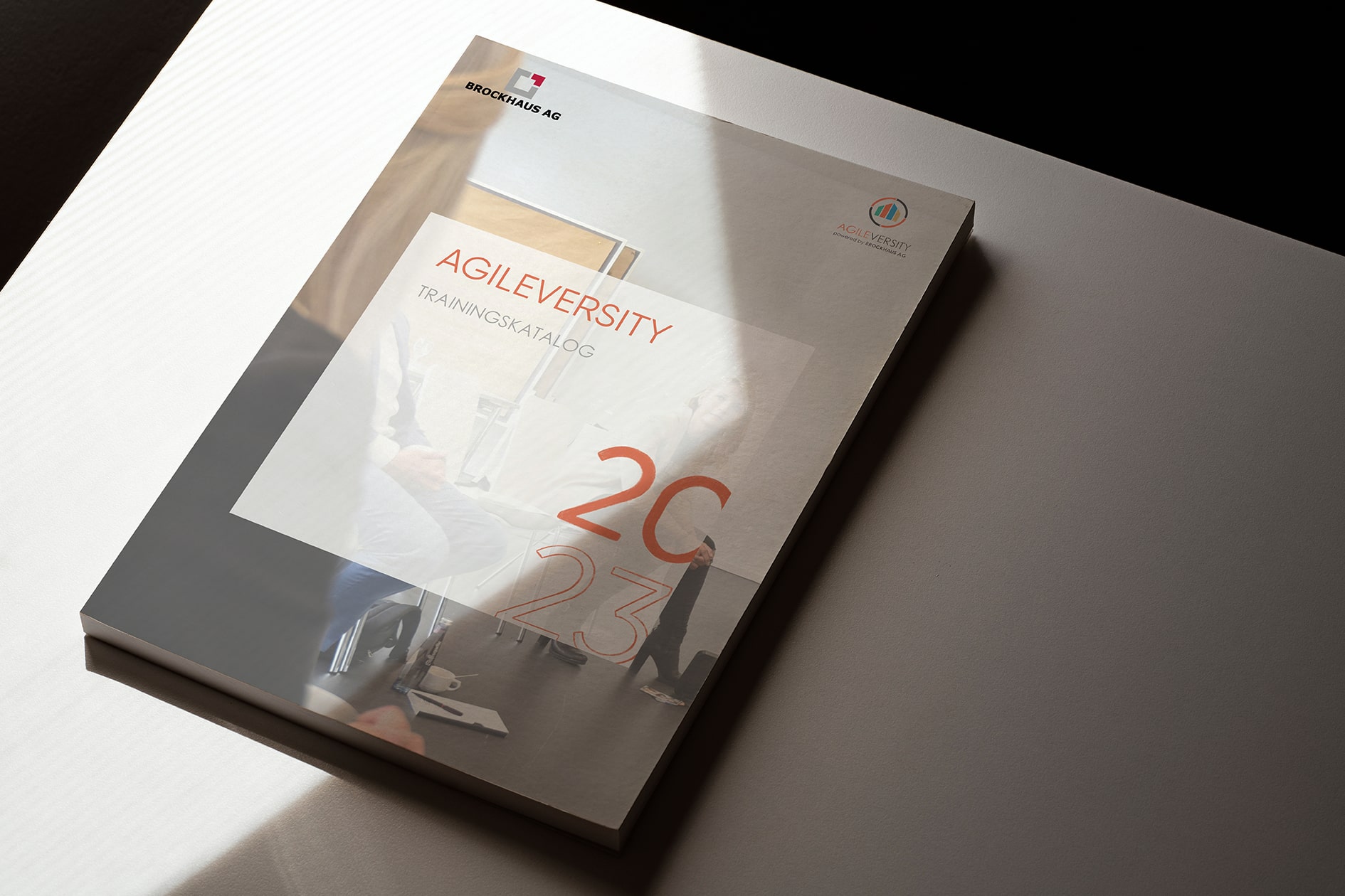 Auf dem Bild liegt der neue Trainingskatalog von AGILEVERSITY für Versicherungsunternehmen auf einem Tisch.