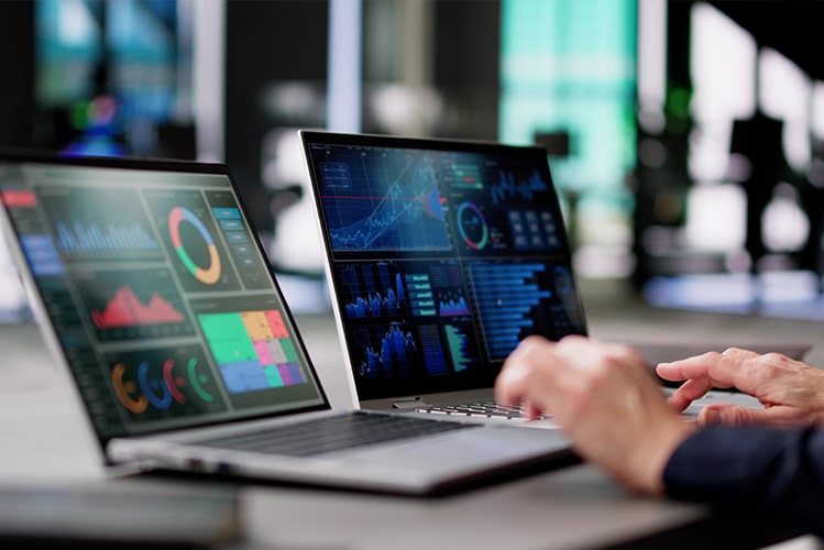 Zwei Hände an einer Tastatur, mit zwei Laptops im Vordergrund, die Analysen und Grafiken einer Datenanalyseplattform für Gas und Strom zeigen.