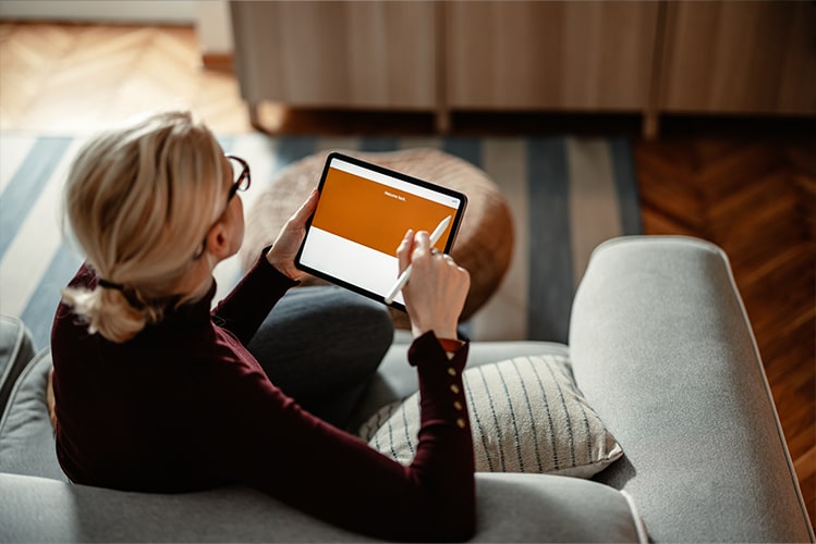 Frau schließt eine Versicherung über eine vollständig digitale Antragsstrecke auf einem iPad ab, bequem von zu Hause auf dem Sofa.