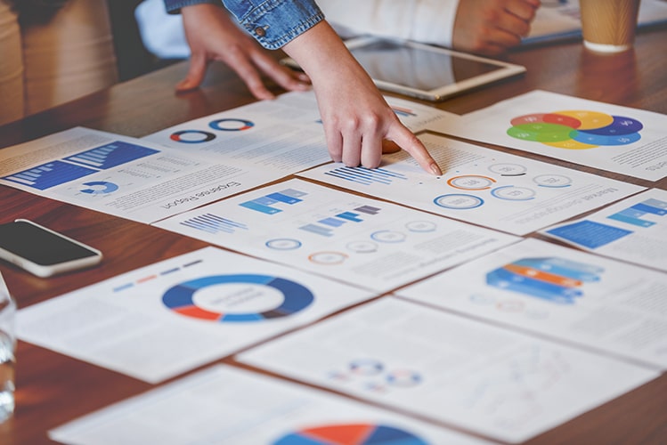 Person zeigt auf Datenvisualisierungen und Diagramme, die auf einem Tisch ausgebreitet sind, während ein Team eine Cloud-native Datenplattform zur Analyse von Einzelrisiken entwickelt.