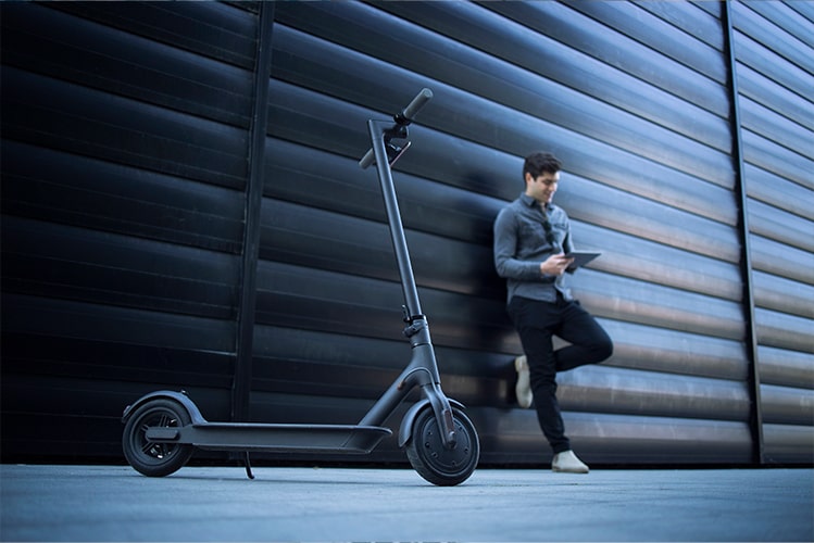 Ein Mann mit iPad in der Hand vor einem E-Scooter, der das digitale Großkundenportal für die automatisierte Policierung von E-Scootern symbolisiert.