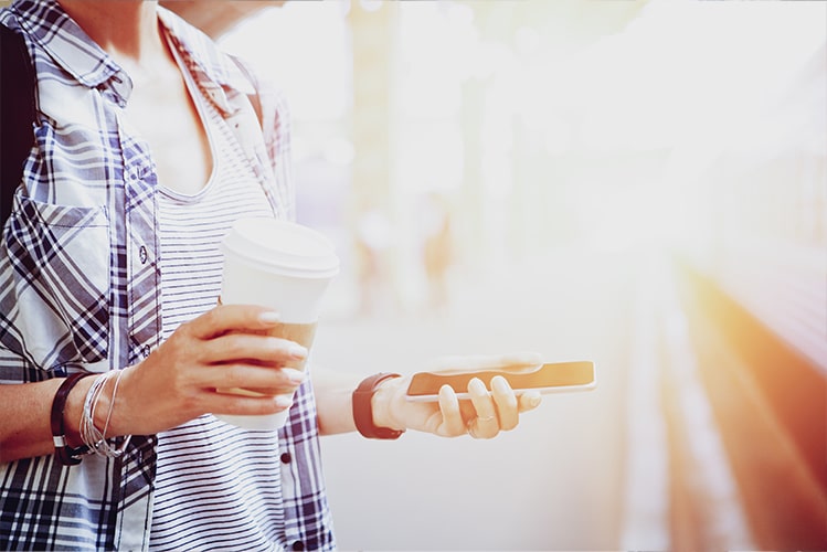 Person am Bahnsteig mit Handy und Kaffeebecher, symbolisiert den MVP-Test einer Reisebegleiter-App mit detailliertem Tracking und Echtzeitdatenanalyse.