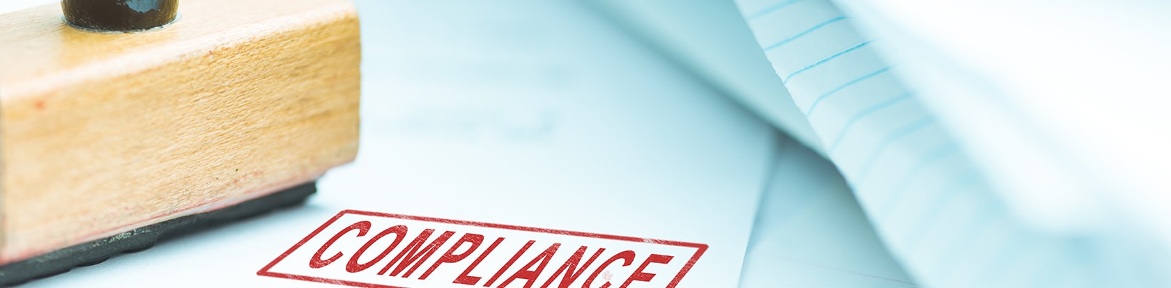 Holzstempel mit dem gestempelten Wort "Compliance" auf einem Blatt Papier, symbolisiert den erfolgreichen Abschluss des BAIT-Compliance-Projekts.