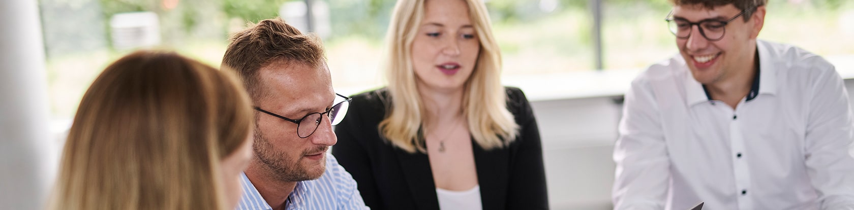 Vier BROCKHAUS AG Mitarbeitende schauen gemeinsam auf ein Projekt, das die Implementierung der BiPRO-Norm für eine effizientere Datenkommunikation im Versicherungswesen umfasst.