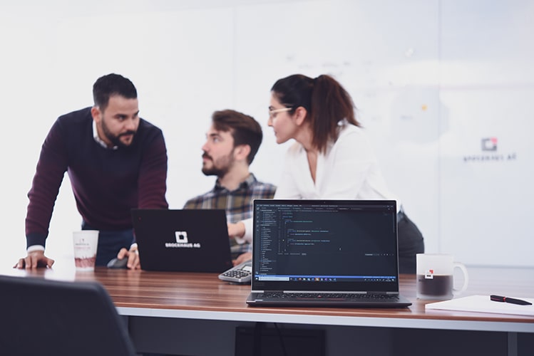 Drei BROCKHAUS AG Mitarbeiter diskutieren am Tisch über Anwendungsmodernisierung, symbolisch für die Innovationsbereitschaft und Fachkompetenz im IT-Bereich für Versicherer.
