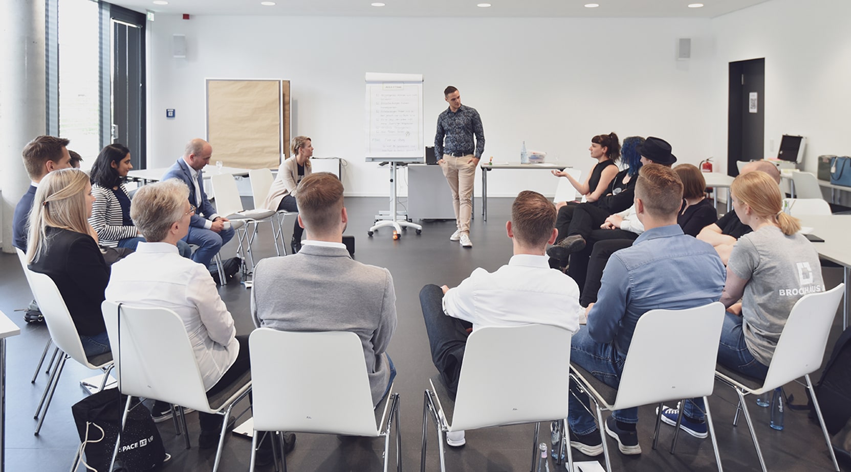 Die Teilnehmer und Teilnehmerinnen des Agileversity Cafés sitzen im Stuhlkreis und hören dem Redner aufmerksam zu.