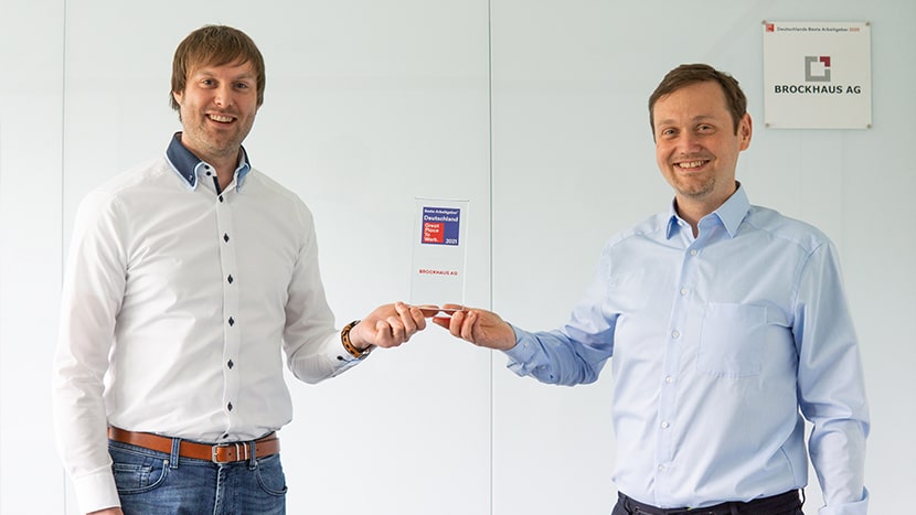 Geschäftleitung der BROCKHAUS AG hält stolz die 'Great Place to Work-Trophäe in die Höhe, feiernd ihren Erfolg als einer von Deutschlands besten Arbeitgebern.