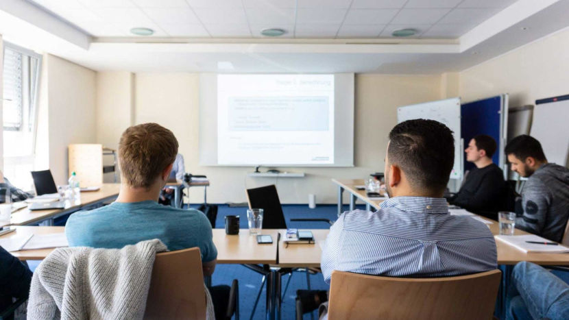 Mitarbeiter der BROCKHAUS AG sitzen in einem Schulungsraum. Zusammen schauen sie auf die Leinwand am Ende des Raumes.