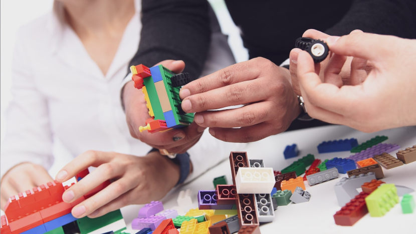Drei Mitarbeiter setzen mit bunten Legosteinen die Produktanforderungen spielerisch um