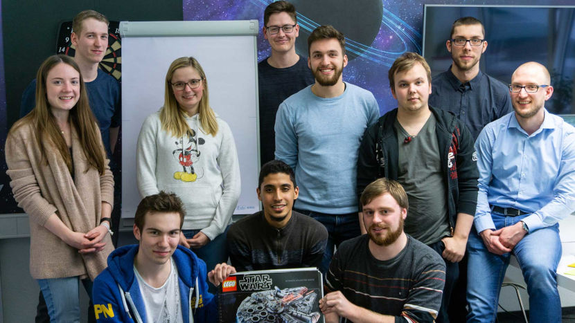 Die Teammitglieder des Scrum-Workshops lächeln in die Kamera und halten den Star Wars Millennium Falcon™ von Lego in den Händen