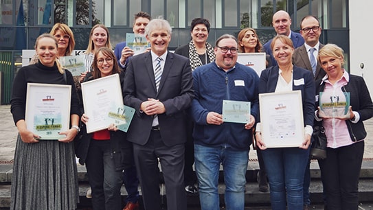 Mitarbeiterin Marie Sonne hält stolz mit den Vertretern weiterer Unternehmen die Urkunde „Pluspunkt Familie“ und die Plakette „Familienfreundliches Unternehmen Kreis Unna 2019“ vom Bündnis für Familie Kreis Unna in die Kamera