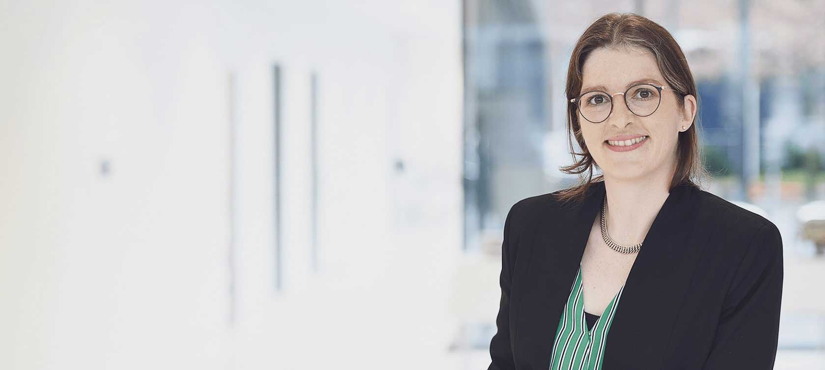 Mitarbeiterin Sarah Hesse steht in einem hellen Raum und lächelt in die Kamera